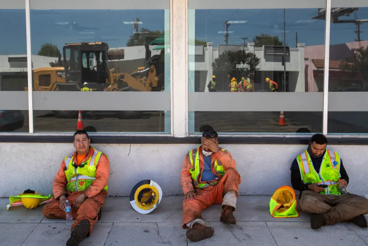 Three construction workers in hi-vis sitting on the ground in the shade during a heat break