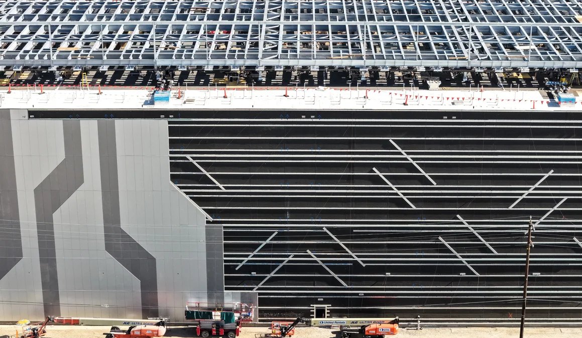 Steel roof framing and cladding on a data center under construction, with lifts working along the wall