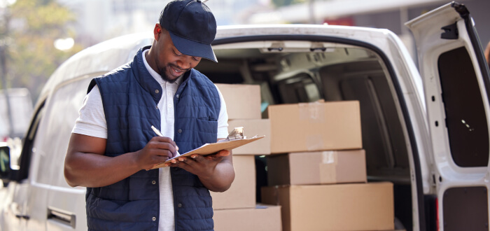 A delivery driver with a clipboard beside an open van full of packages