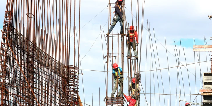 Ironworkers in hard hats climbing and working on tall rebar cages against a blue sky