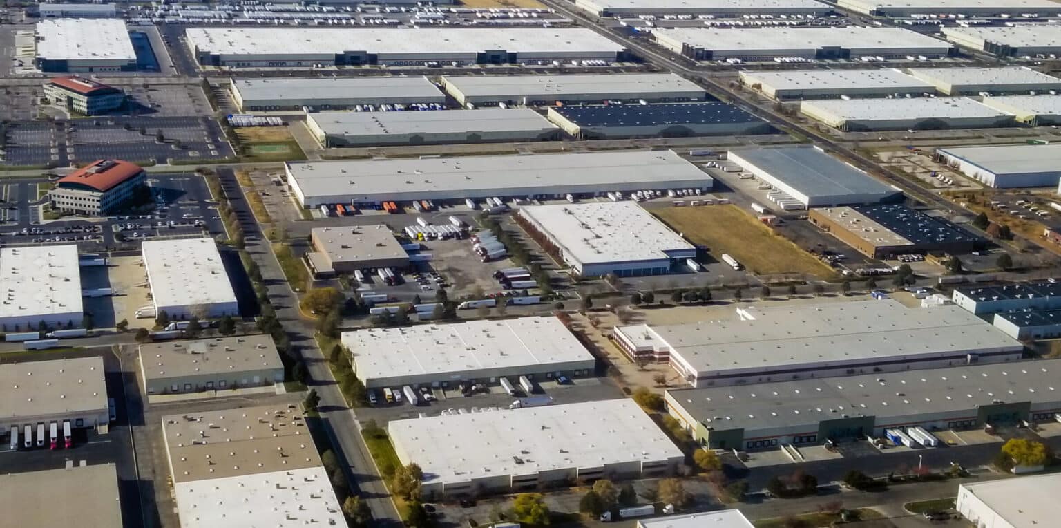 Rows of distribution centers seen from above, dark roofs loading heat all day