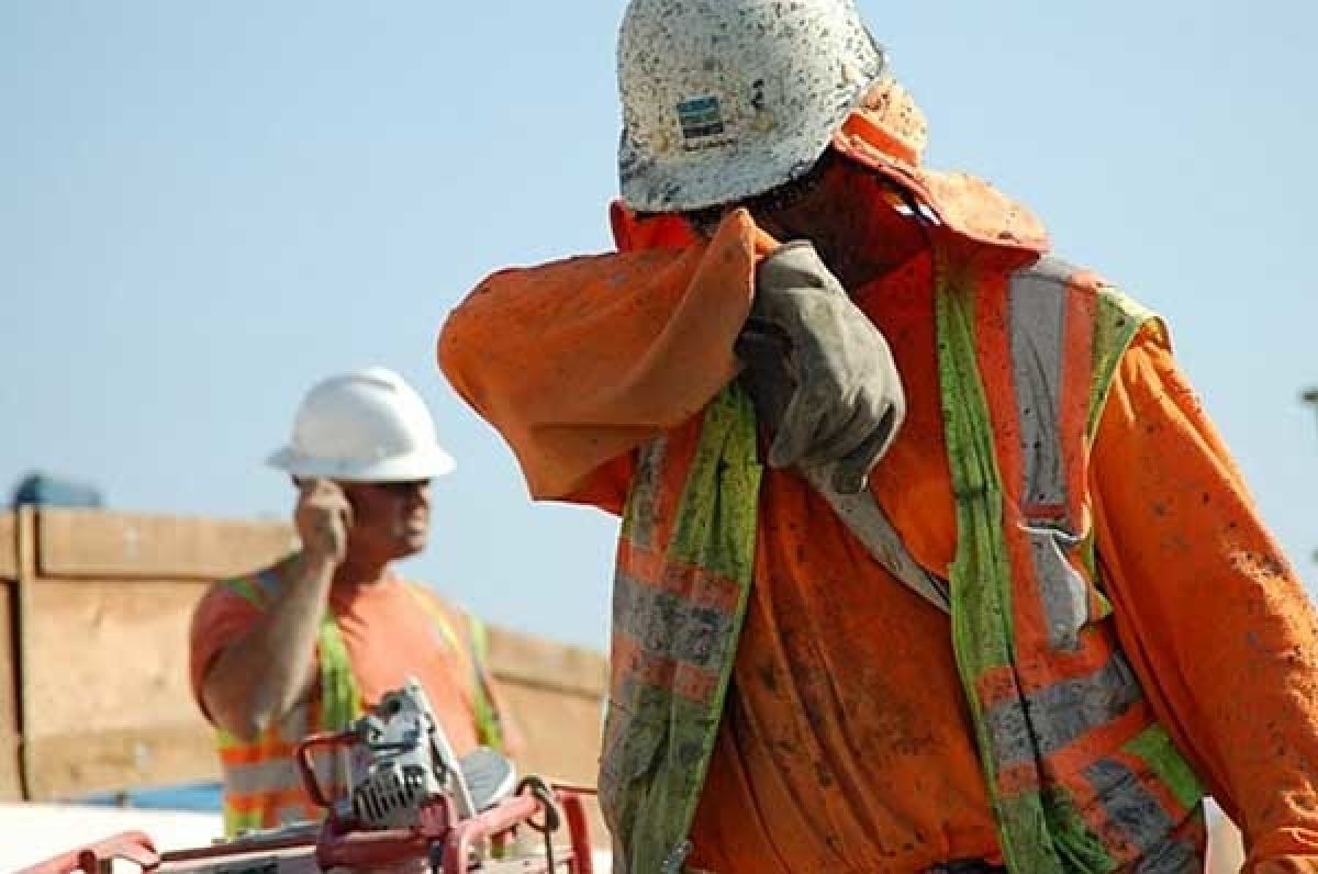 A worker in a hard hat wiping sweat from his face in the sun